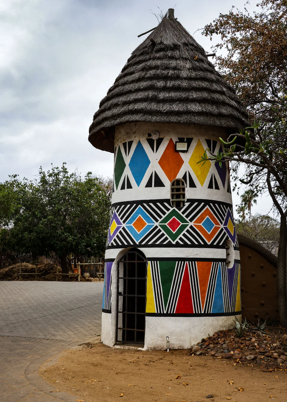 A round homestead with a thatched roof painted in bold Ndebele geometric patterns (representative photograph of Ndebele architecture, not Lesedi's own homestead)